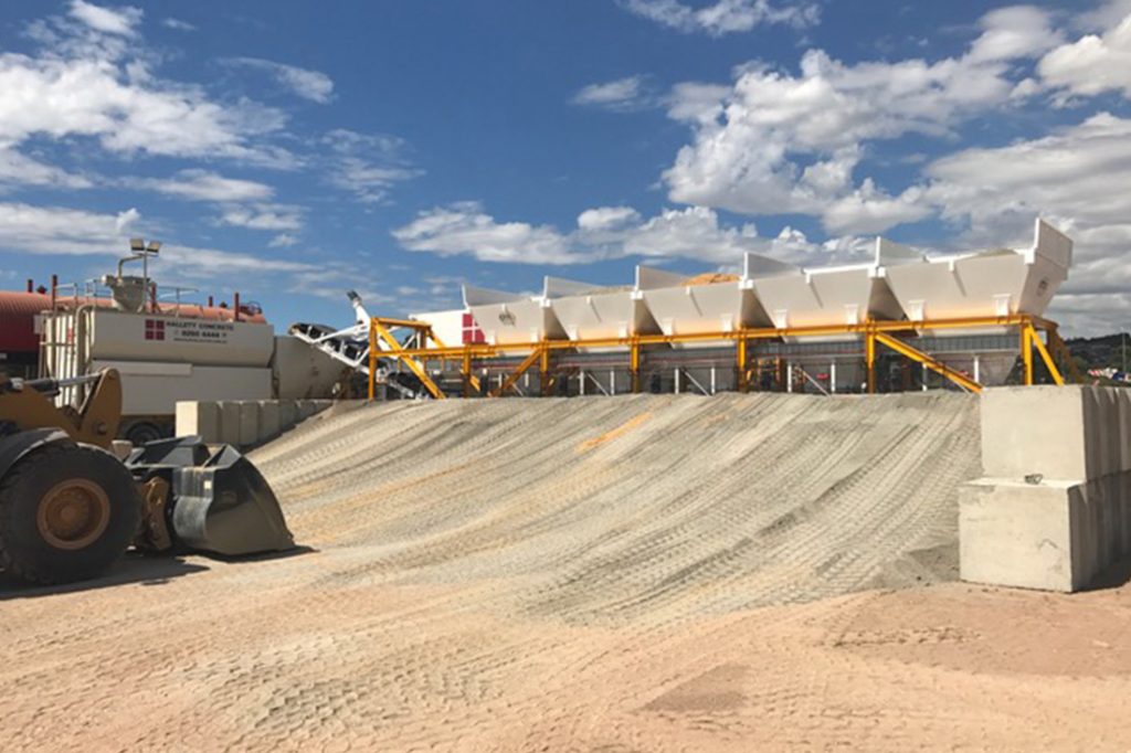 Photo of a sand bank at a processing yard with equipment behind it | featured image for Aggregate Belt Weighers.